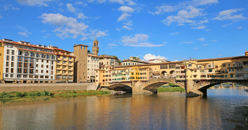 Arch bridge over river by buildings in city against sky