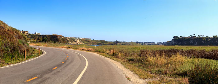 Road by landscape against clear blue sky