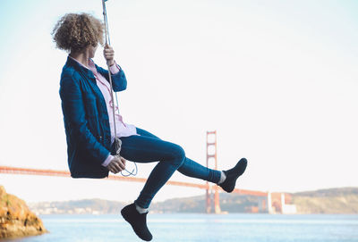 Woman sitting on swing with golden gate bridge in background