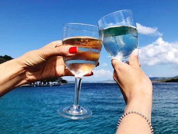 Cropped hands celebrating toast against sea