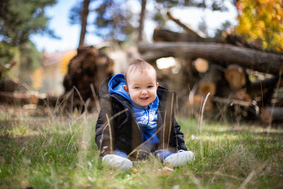 Portrait of boy sitting on grass against trees