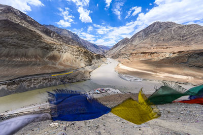 Scenic view of prayer flag by river and mountains against sky