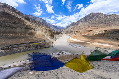 Scenic view of prayer flag by river and mountains against sky