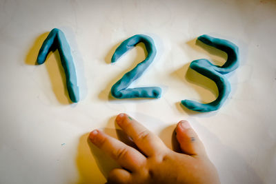 Cropped hand making numbers with modelling clay on white table