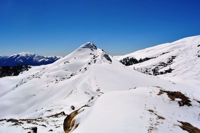 Scenic view of snow covered mountains against clear blue sky