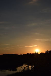 Silhouette trees on landscape against orange sky