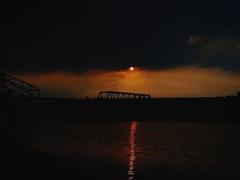 Silhouette bridge over river against sky at sunset