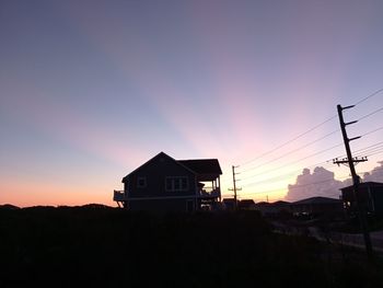 Silhouette house by building against sky during sunset