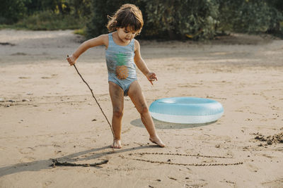 Cute girl drawing with stick on sand at beach