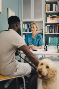 Young man with dog talking to female veterinarian at desk in medical clinic