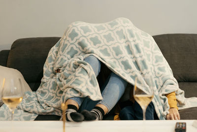 Mother and daughter hiding under blanket on sofa in living room at home