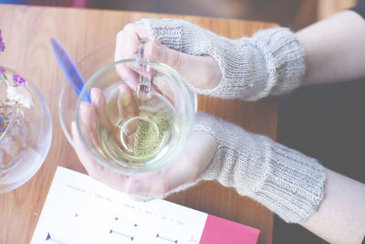 Cropped image of woman wearing mitten holding tea cup at cafe