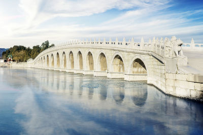 Arch bridge over river against cloudy sky