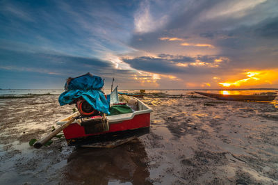 Fishing boat moored at beach against sky during sunset