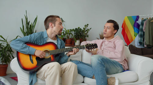 Man playing guitar while sitting on sofa at home