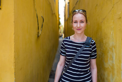 Portrait of smiling young woman standing against yellow wall