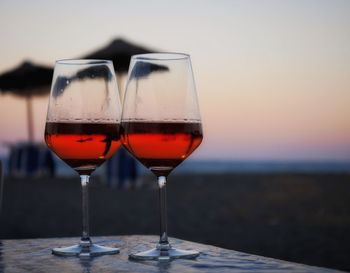 Wineglasses on table at beach against sky during sunset