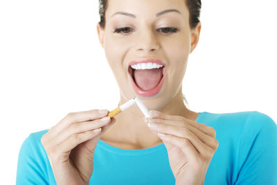 Smiling young woman breaking cigarette against white background