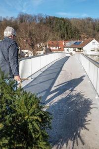 Senior man pulling branches in cart on footbridge during sunny day 