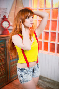 Thoughtful young redhead woman with hand in hair standing in room