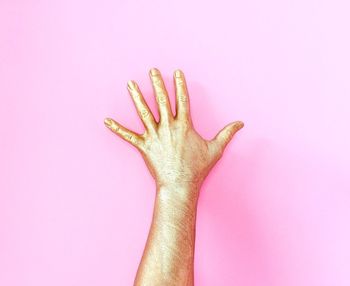 Cropped image of gold painted hand against pink background