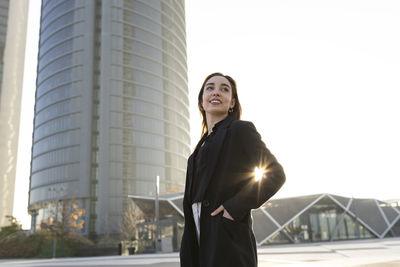 Smiling businesswoman with hand in pocket looking away while standing in city