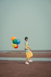 Full length of young woman holding colorful balloons at beach