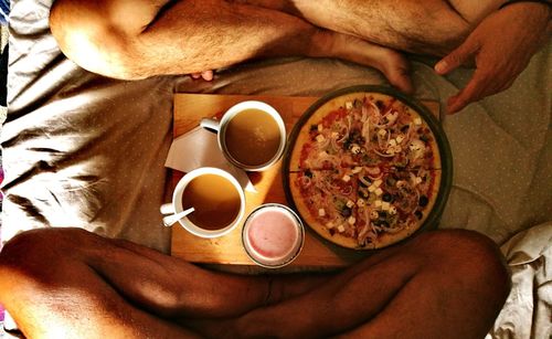 Low section of friends having pizza with coffee on bed