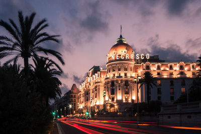 Illuminated building by road against sky at night