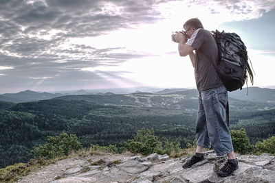 Man holding camera at eye on mountain and takes photos. man watching sunset through viewfinder