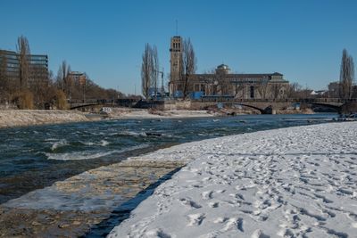 View of frozen river in city against clear blue sky