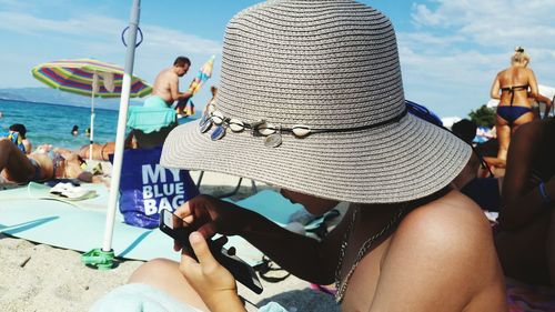 Close-up of woman wearing hat using mobile phone while sitting on beach