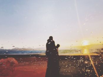 Silhouette woman on glass window against sky during sunset