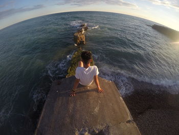Fish-eye view of man sitting on rock formation against sea