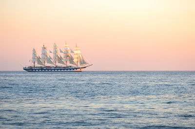 Sailboat sailing in sea against clear sky during sunset