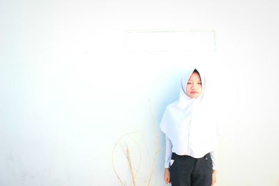 Portrait of young woman standing against white wall