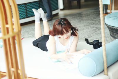 Young woman reading book while lying on mat at home