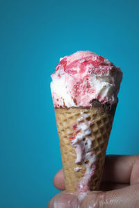 Close-up of hand holding ice cream cone against blue sky