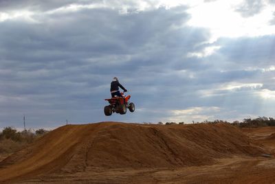 Man jumping quadbike over sand against cloudy sky