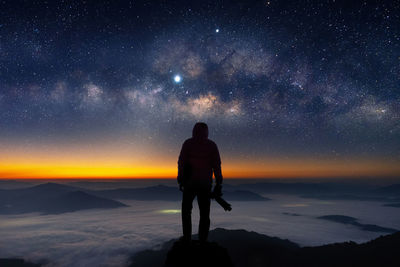 Rear view of man standing on field against sky at night