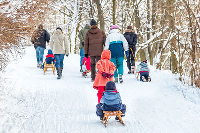 Rear view of people tobogganing on snow covered field