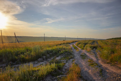 Road amidst field against sky during sunset