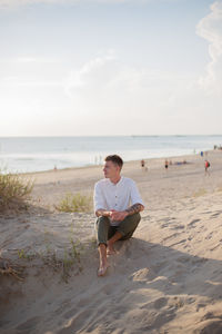 Side view of woman sitting on beach against sky