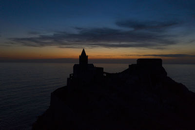 Silhouette building by sea against sky during sunset