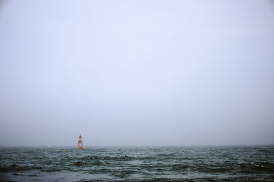 Lighthouse by sea against clear sky