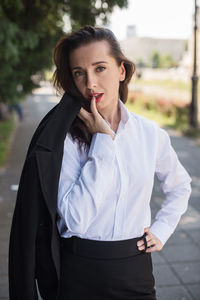 Portrait of beautiful businesswoman holding suit while standing on footpath