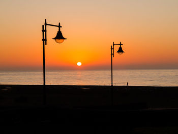 Silhouette street lights on promenade against orange sky