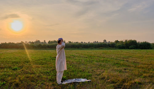 Woman standing on field against sky during sunset