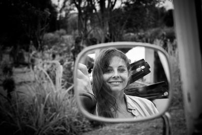 Portrait of smiling young woman reflecting on side-view mirror