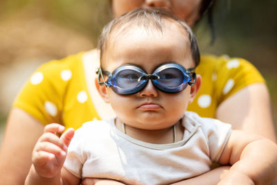 Midsection of mother holding cute daughter wearing swimming goggles while sitting outdoors